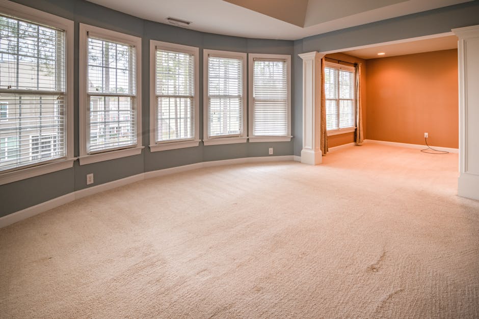 A professional cleaner from Deep Cleaning Croydon dressed in a full white protective suit, mask, and gloves is performing deep cleaning and sanitisation of a beige carpet using a steam cleaning machin